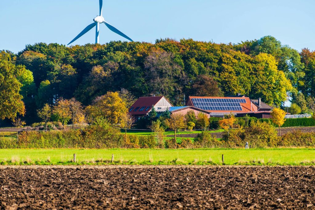 Boerderij met zonnepanelen en windmolen achter bos in landelijk gebied