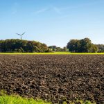 Omgeploegd landbouwveld met bomen aan de rand onder heldere blauwe lucht